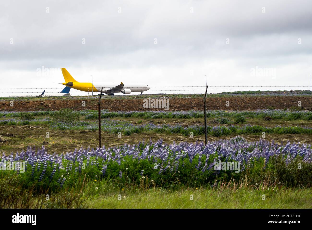 Frachtflugzeug steht am Anfang einer Start- und Landebahn, die an einem bewölkten Sommertag starten kann. Ein rollende Passagierflugzeug ist im Hintergrund sichtbar. Stockfoto