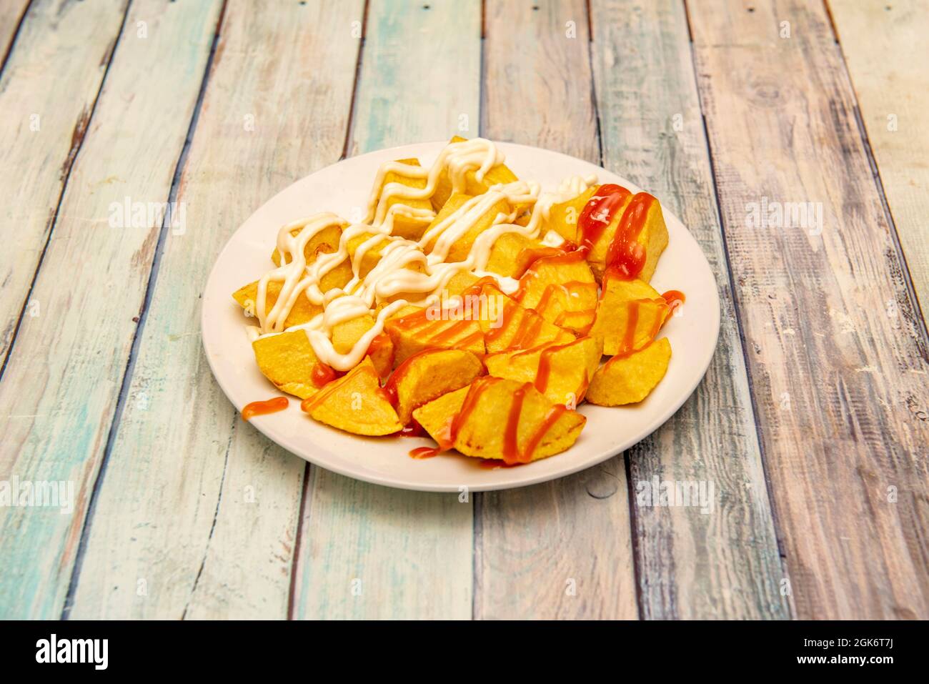 Gebratene Kartoffeln in Würfel mit brava-Sauce und Aioli, die in einer Tapas-Bar in Madrid auf einem hölzernen Hintergrund zubereitet werden Stockfoto