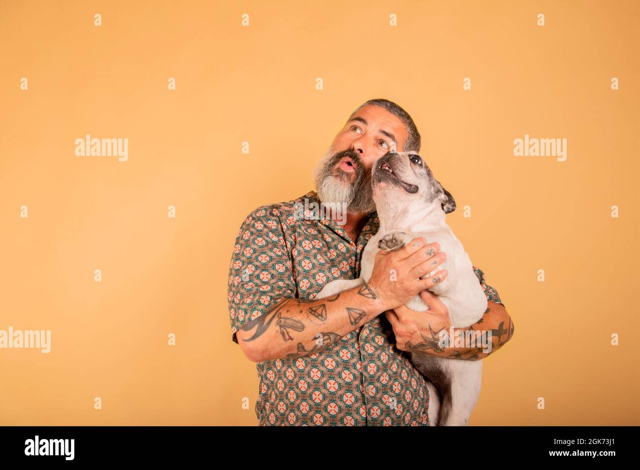 Ein Studioporträt eines bärtigen Mannes, der seinen Hund mit einem erstaunten Gesicht auf dem Arm hält Stockfoto