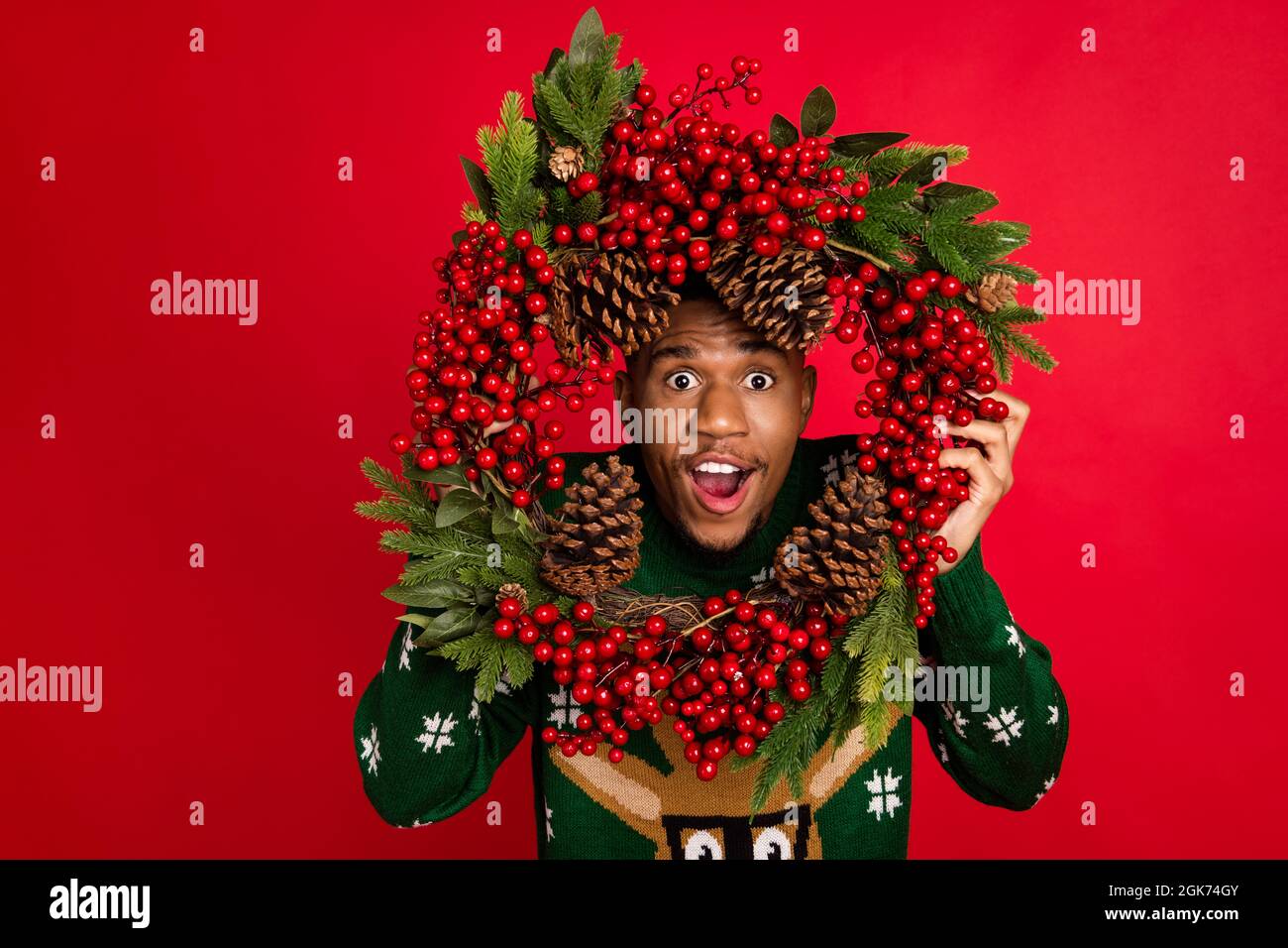 Portrait von attraktiven fröhlich erstaunt Kerl halten Blick durch festal Kranz benutzerdefinierte isoliert über hellen roten Hintergrund Stockfoto