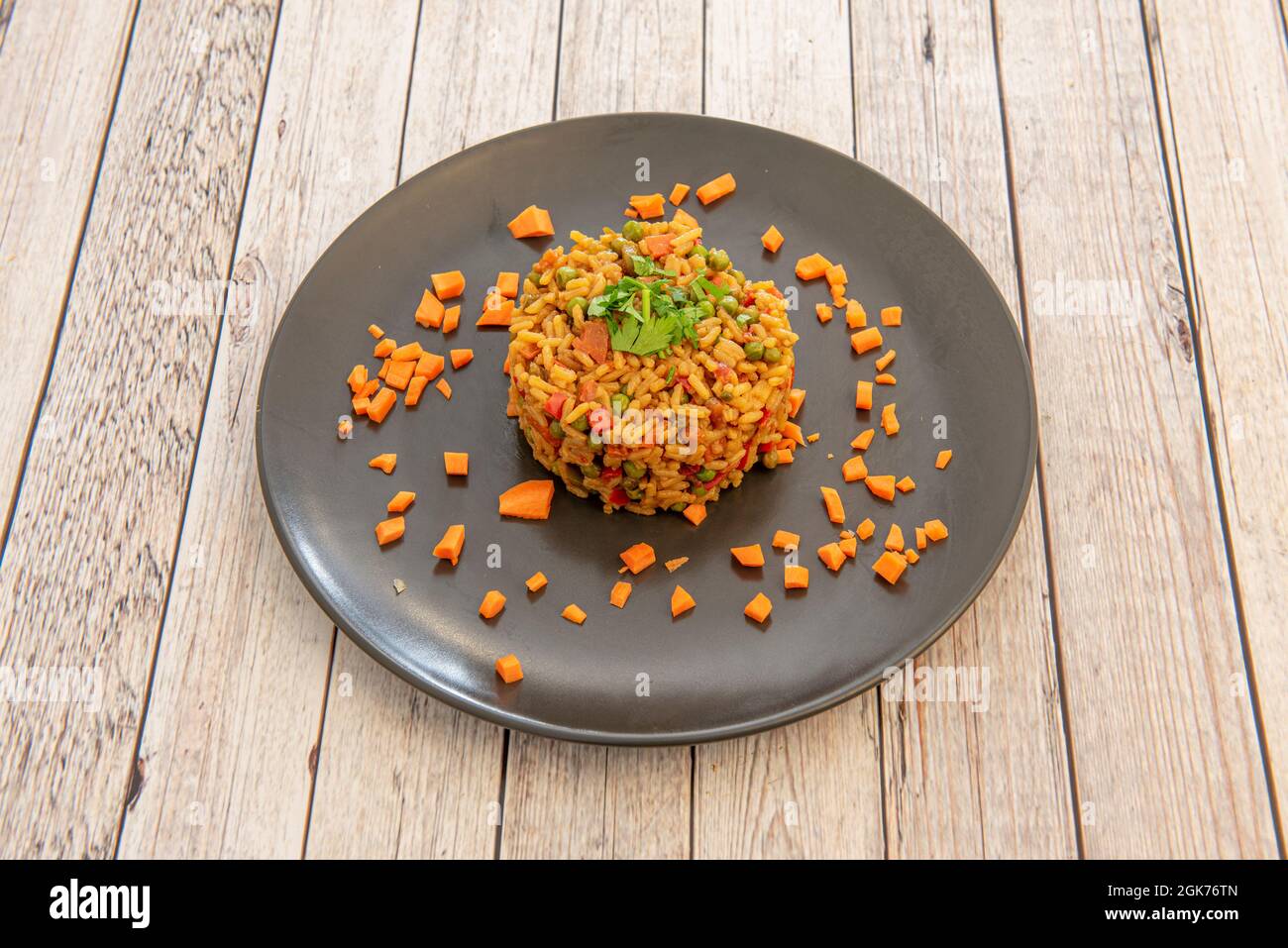 Reis mit Gemüse mit Erbsen, Petersilie, Paprika und Karotten auf schwarzem Teller Stockfoto