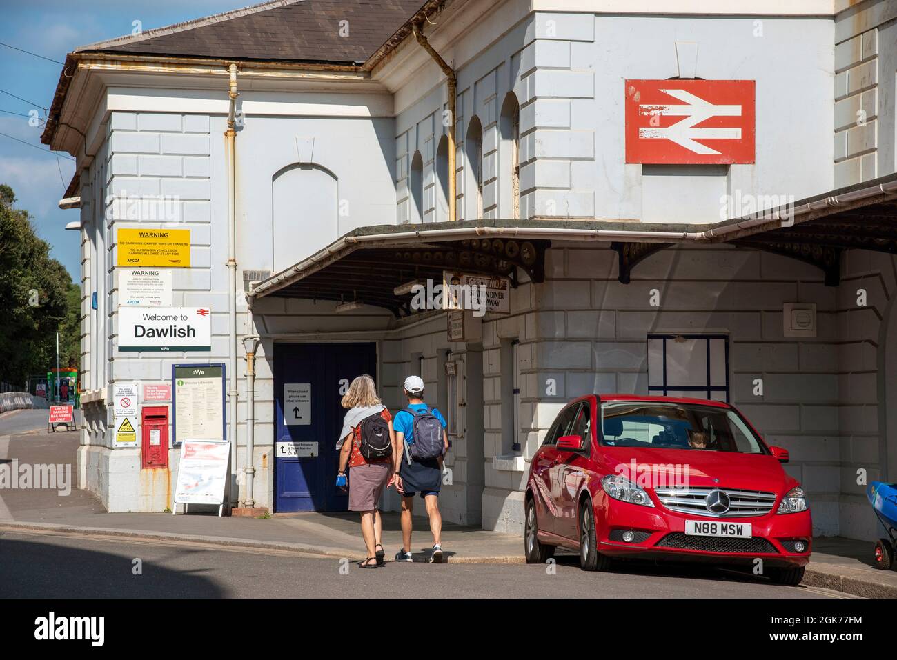 Dawlish, Devon, England, Großbritannien. 2021. Dawlish Badeort Bahnhof Gebäude, eine Außenansicht mit geparktem Auto und Passagiere. Stockfoto
