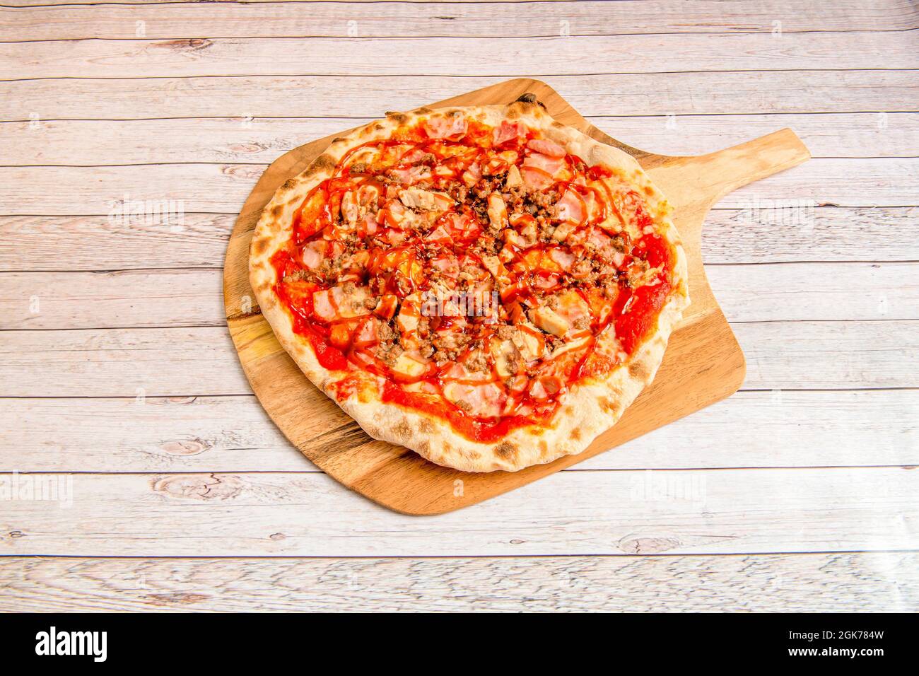 Großer italienischer Koch Zubereitung von Pizza mit dünner Kruste mit Barbecue-Sauce mit gehacktem gebratenem Huhn, Schinkenscheiben geschmortes Hackfleisch auf Holzbrett Stockfoto
