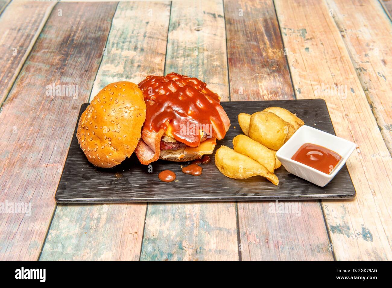 Rindfleisch-Burger mit Käse und Speck und viel Grillsoße, Brötchen mit Sesam und Pommes frites. Stockfoto