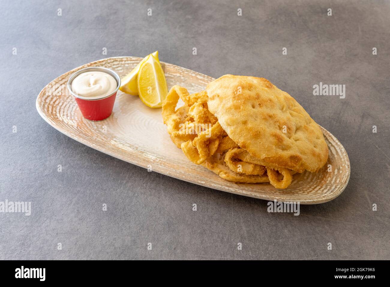 Muffin mit Tintenfischringen, in Ei und Mehl zerschlagen und in Olivenöl mit Mayonnaise und Zitronenkeilen gebraten Stockfoto