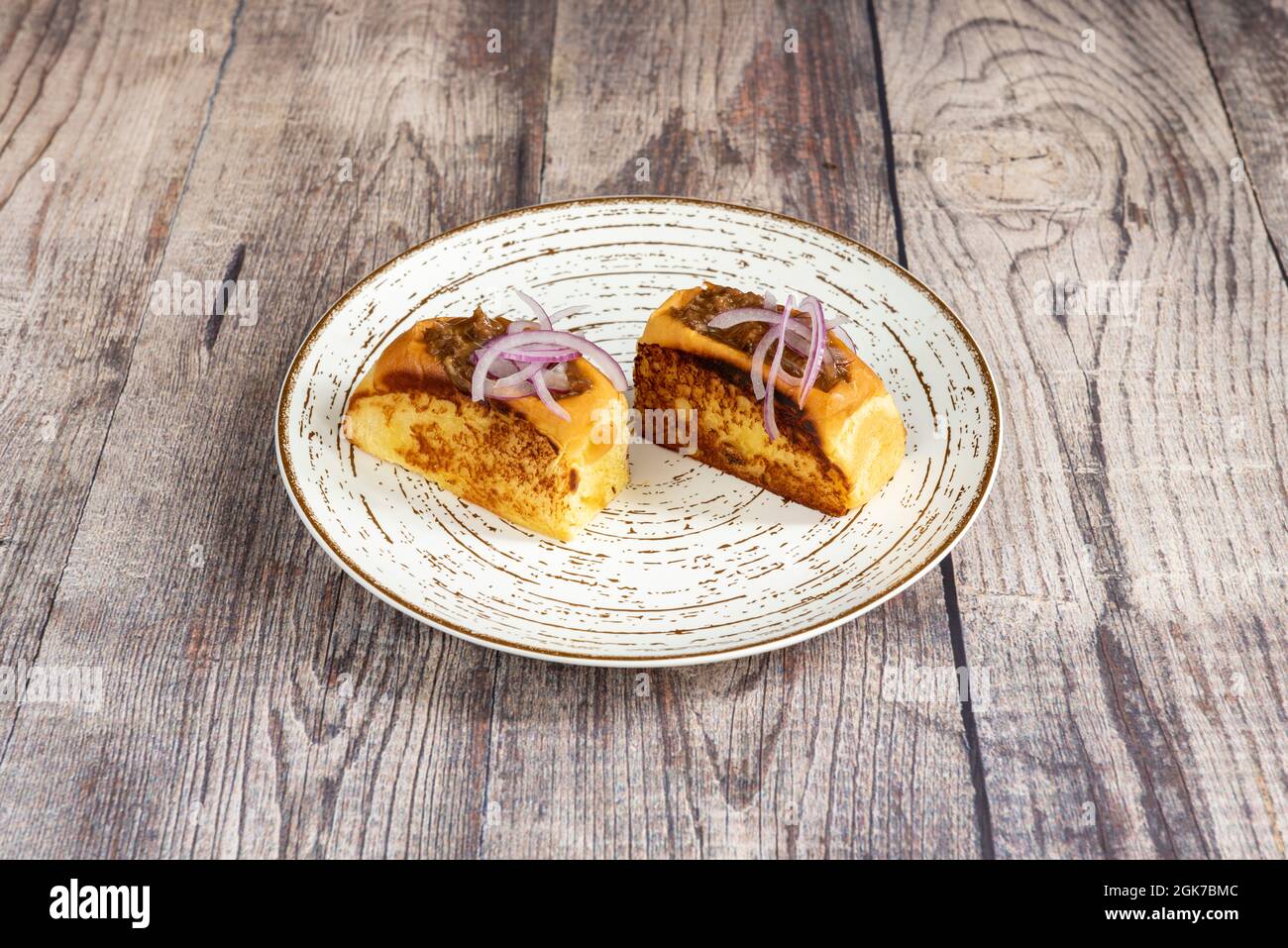 Geröstetes Brioche-Brot, gefüllt mit Schweinefleisch im spanischen Stil und darauf kleine Stücke lila Zwiebel auf einem weißen Teller Stockfoto