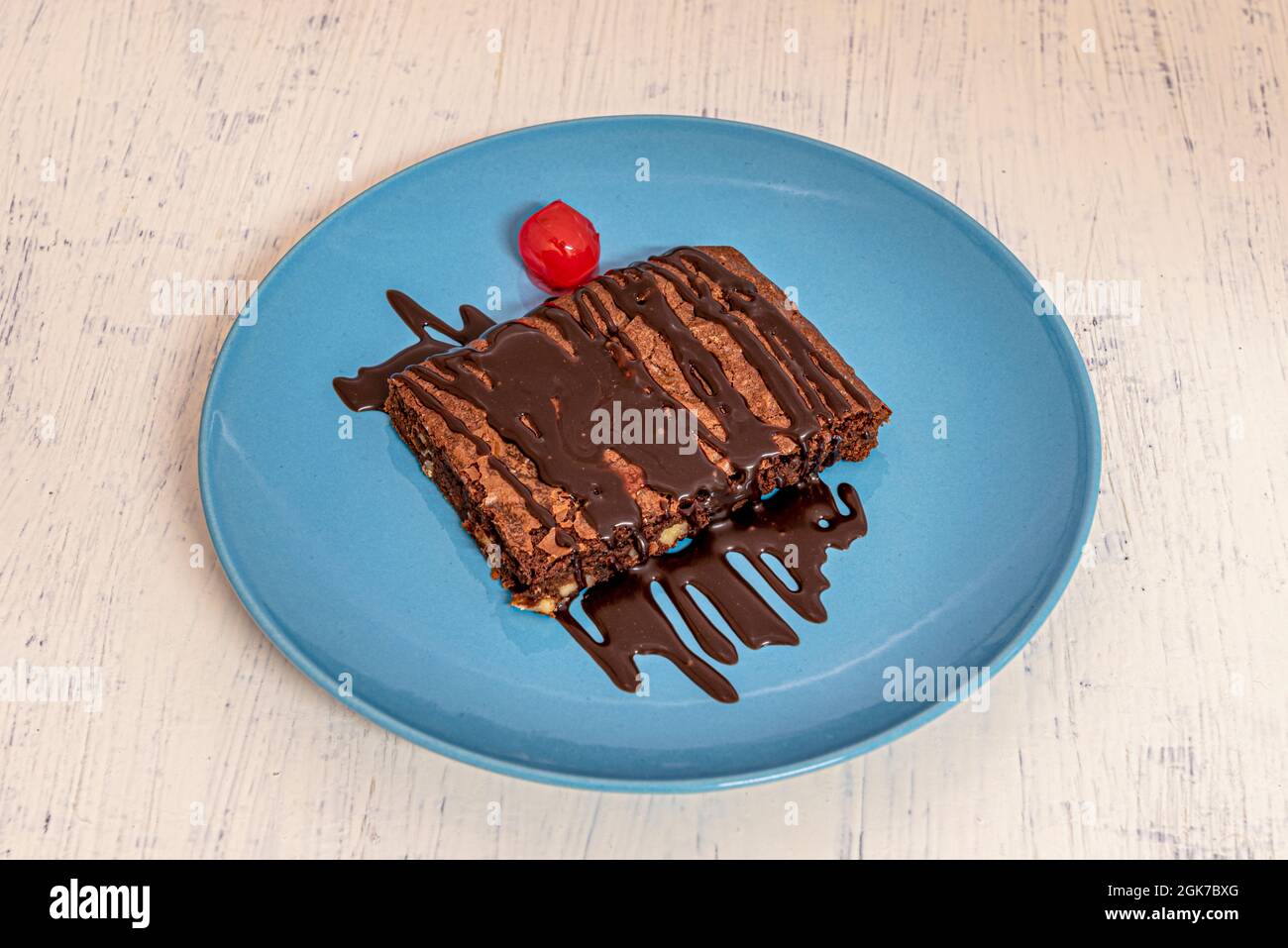 Große Portion Brownie-Kuchen mit Nüssen und viel Schokoladensirup auf der Oberseite mit einem sirupartig vereißenen auf einem blauen Teller Stockfoto