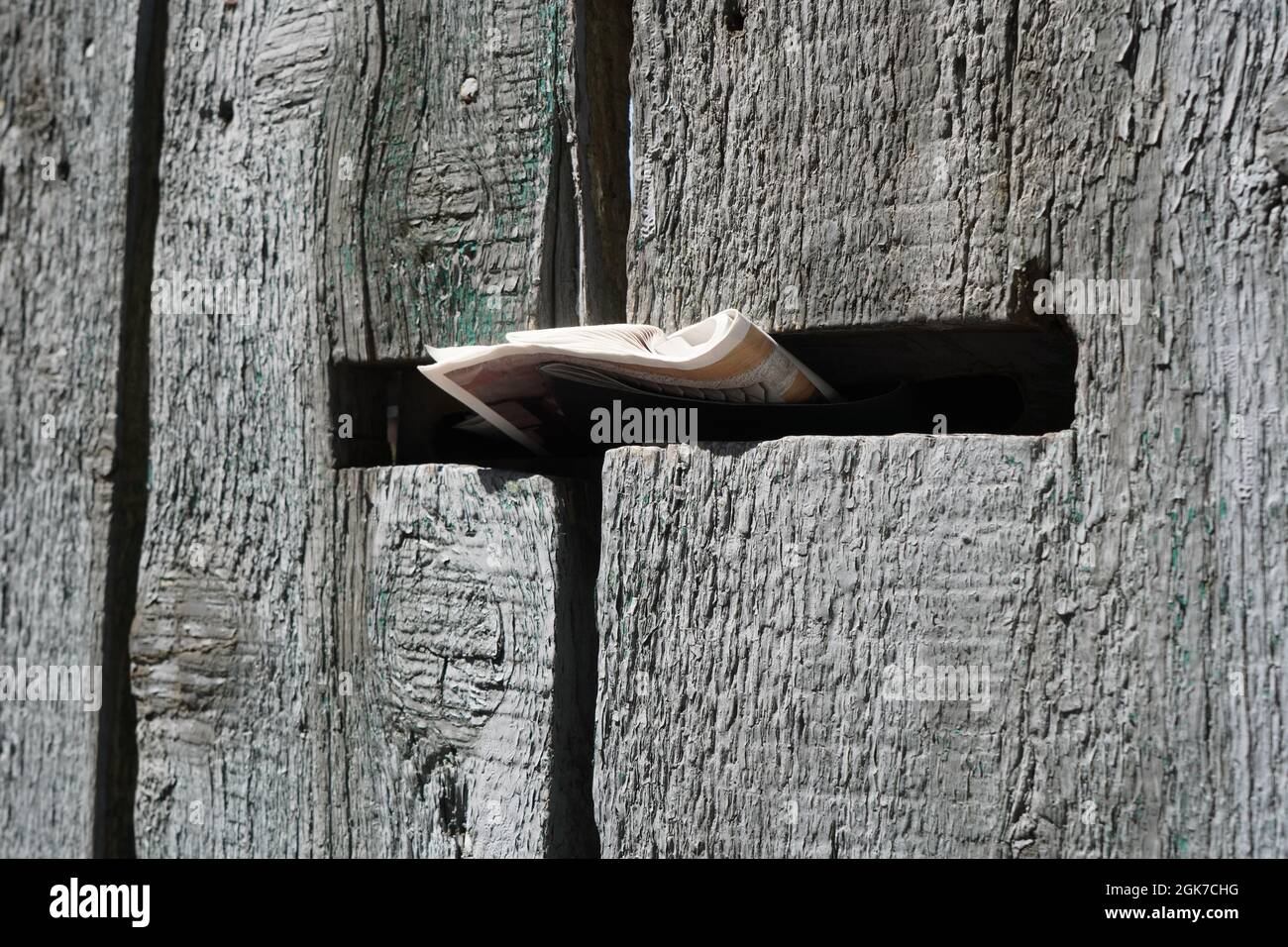 Rustikaler alter Zaun aus robusten Naturholzplatten mit Briefkasten darauf angebracht und Werbebroschüre im Briefkasten Stockfoto