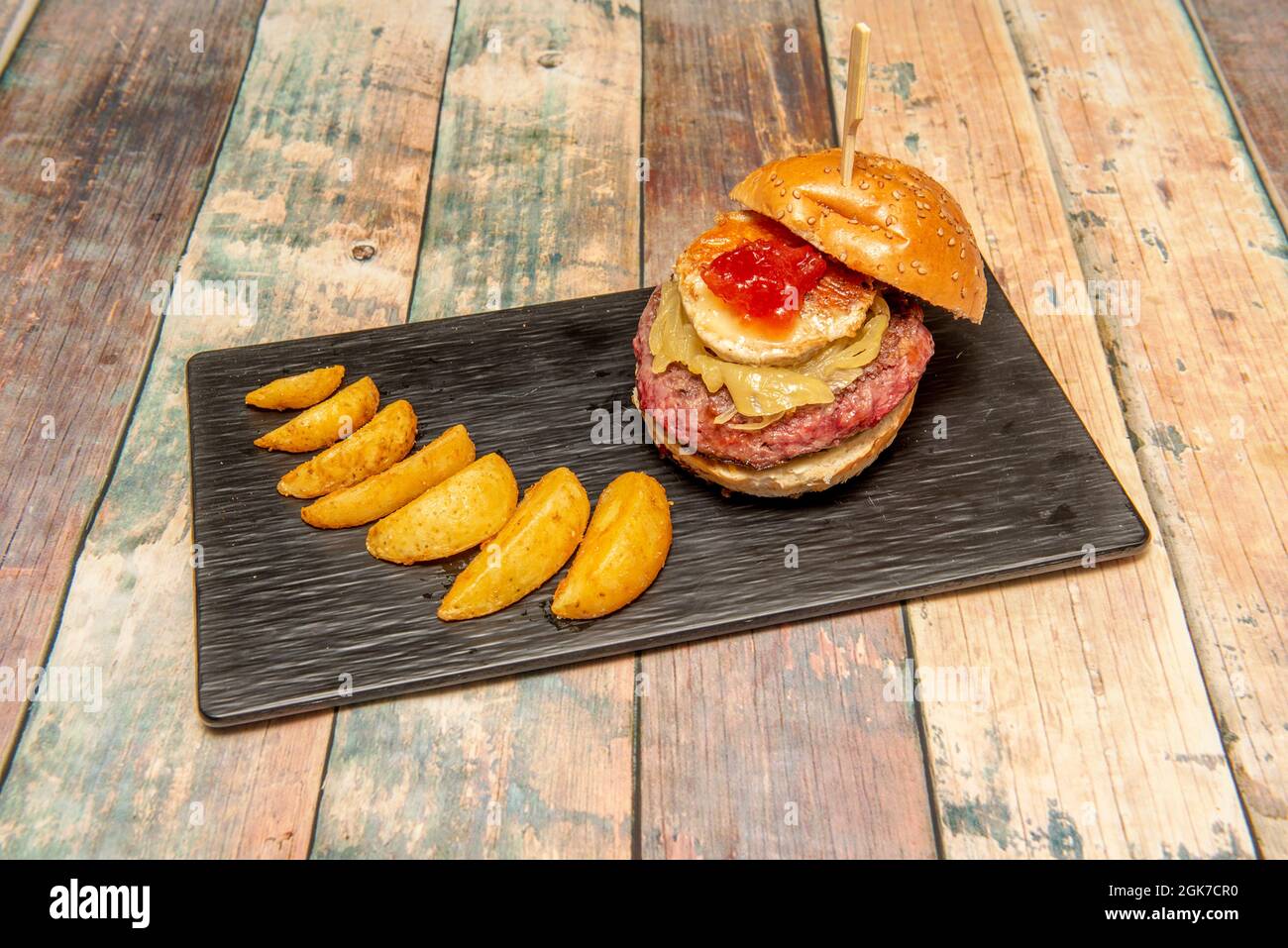 Köstlicher Rinderburger mit Sesambrot, Zwiebeln, Ziegenkäse, Tomatenmarmelade und Pommes frites Stockfoto