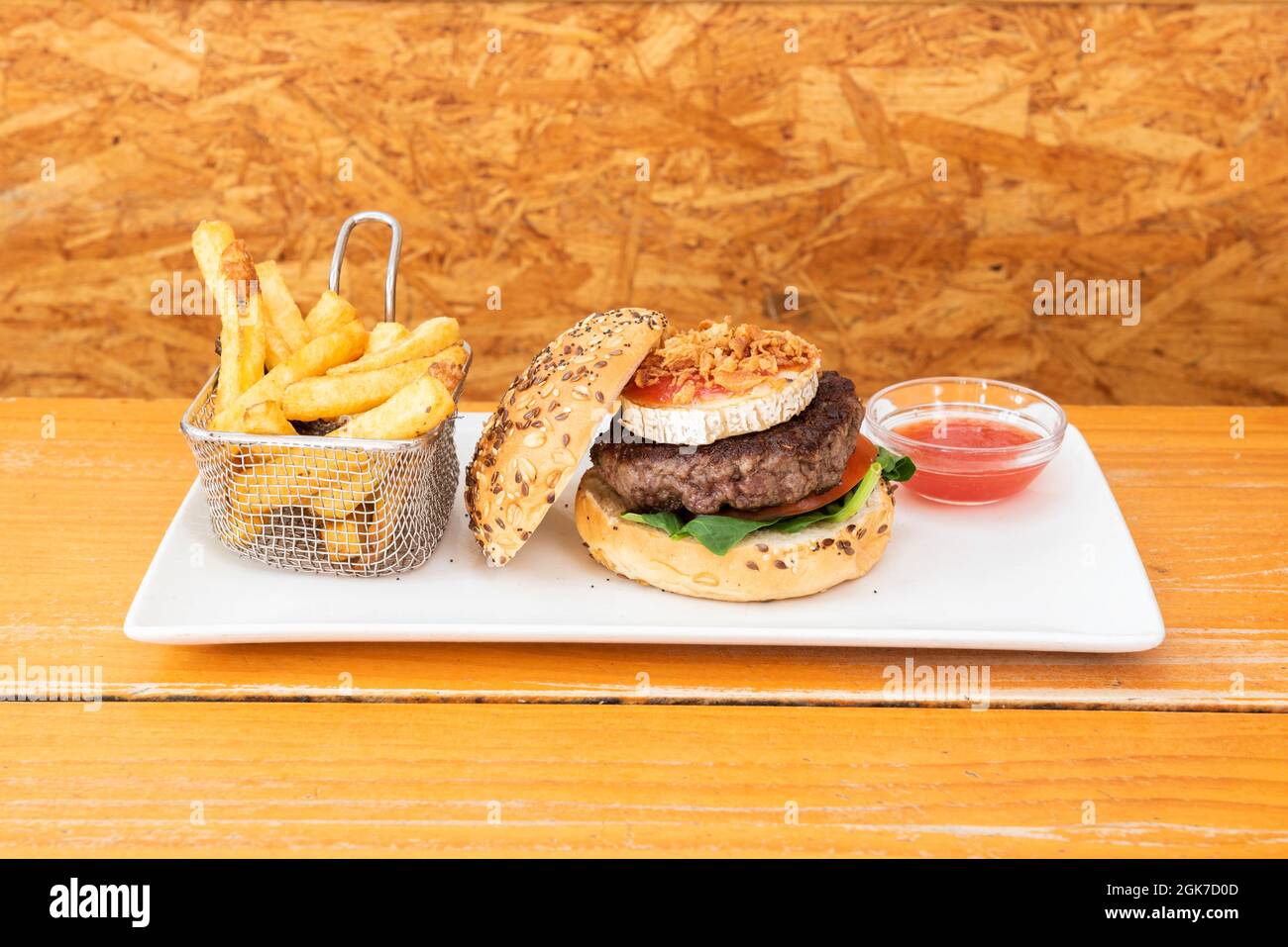 Köstlicher Rindfleisch-Burger mit einer Scheibe Ziegenkäse, Tomatenmarmelade, knuspriger Zwiebel, Spinatblättern, Brot mit Samen und einer Seite Pommes frites Stockfoto