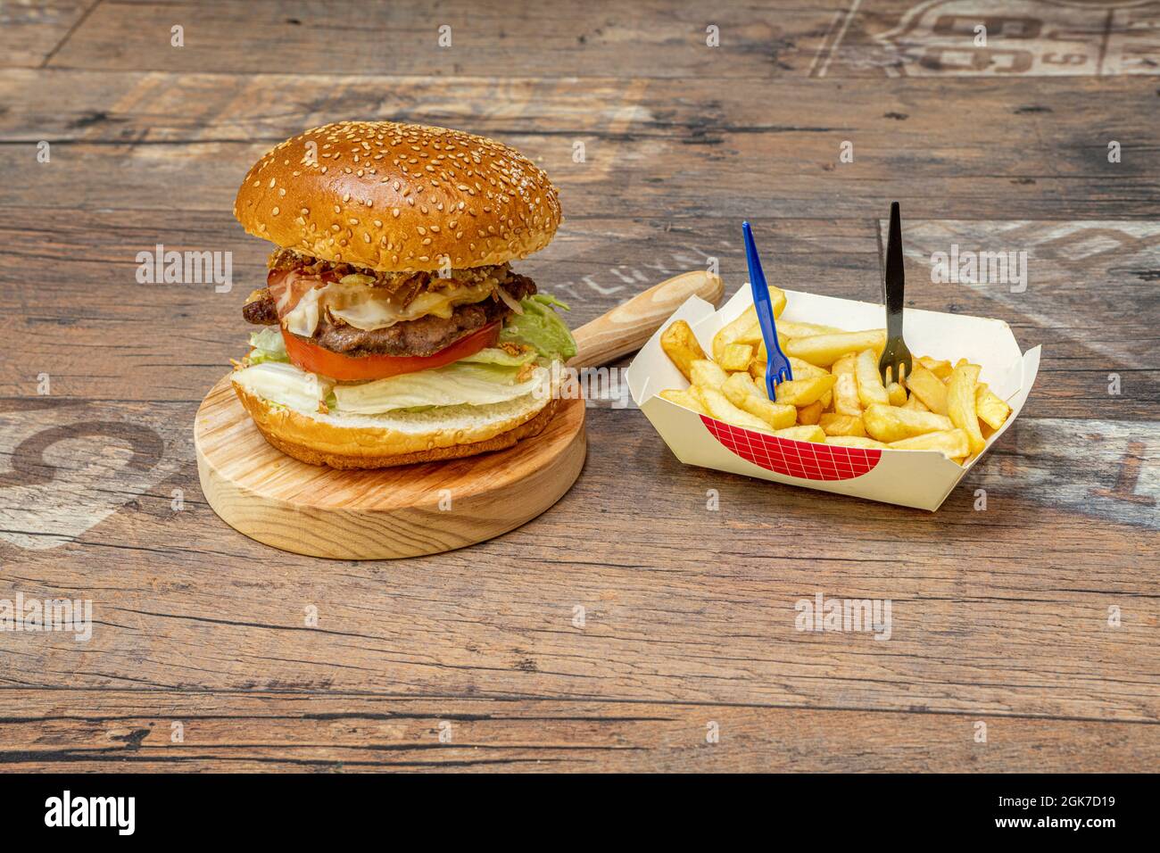 Klassischer Rindfleischburger mit Brot mit Sesamsamen, Tomaten und Salat und gebratenen Schinkenauflagen mit gebratener Zwiebel mit Pommes als Garnitur Stockfoto