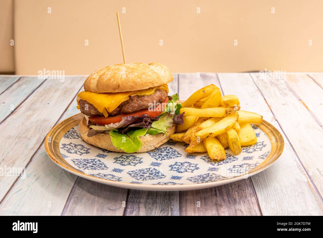 Klassischer Rindfleischburger mit Salat, geschmolzenem Cheddar-Käse, Tomatenscheibe, Mayonnaise und hausgemachten Pommes frites Stockfoto