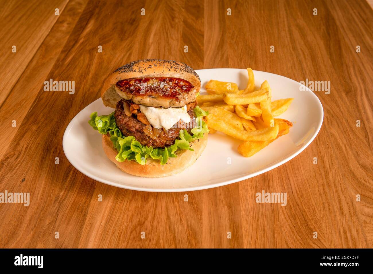 Rindfleisch-Burger mit einem Stück Gänseleberpastete am Rand, Salat, Sauce, karamellisierter Zwiebel und Beilage-Pommes Stockfoto