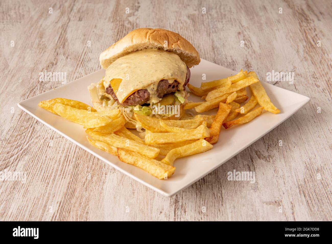 Rinderburger mit Käse, Cheddar-Sauce, Salat, Gurken und garniert mit Pommes frites Stockfoto