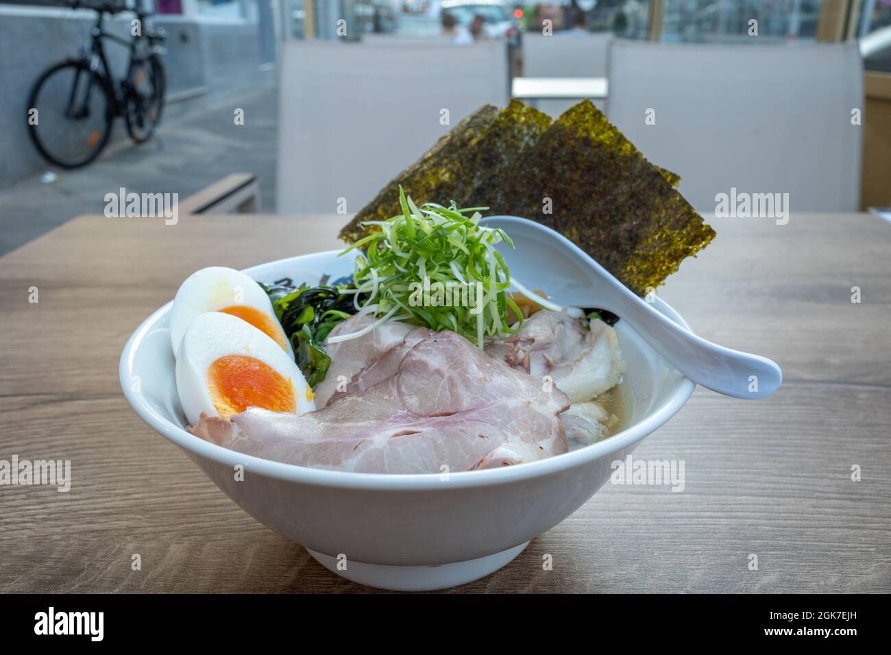 Shio Ramen, japanische Nudellattenmuscheln-Suppe, darauf Schweinefleisch, gekochtes Ei, Bambussprossen, rote Zwiebel und Nori, auf einem hölzernen Außentisch. Stockfoto