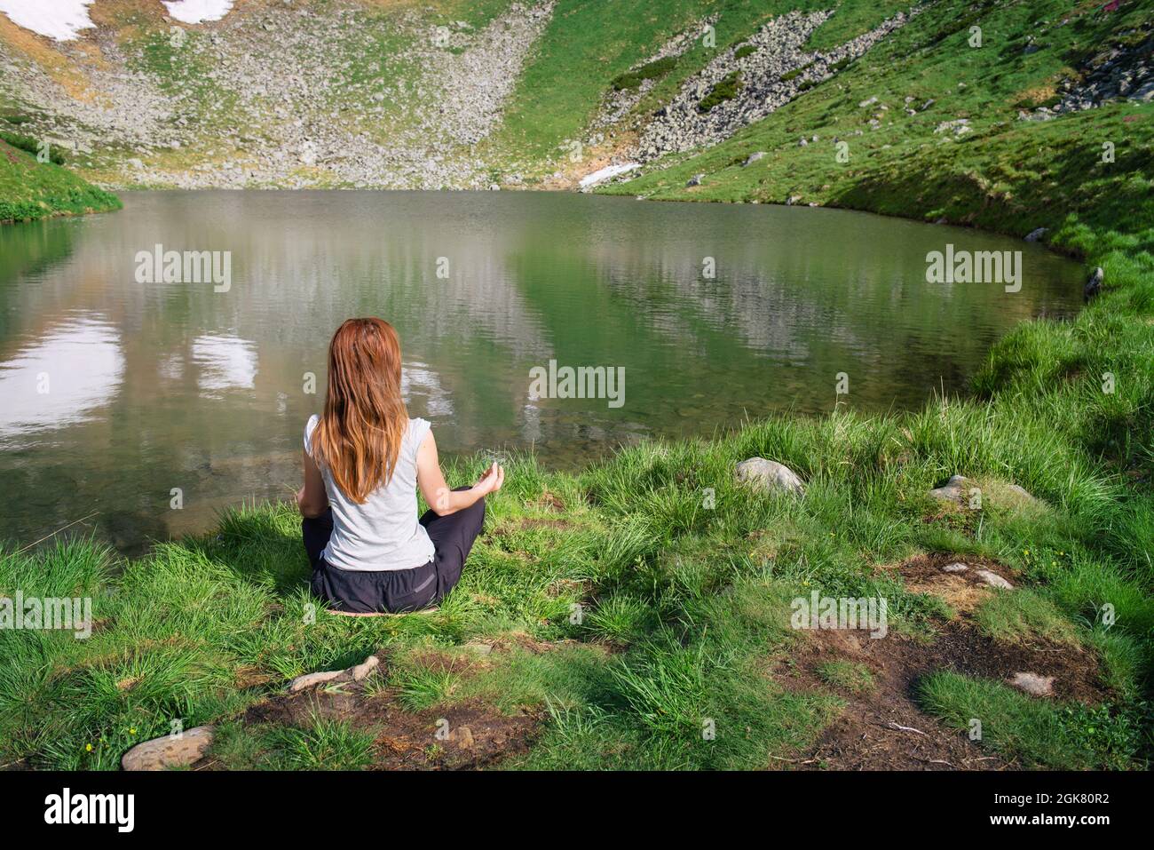 Attraktive junge Frau genießt die Natur und praktiziert Yoga vor dem Bergsee. Rückansicht. Gesundes Lifestyle-Konzept Stockfoto