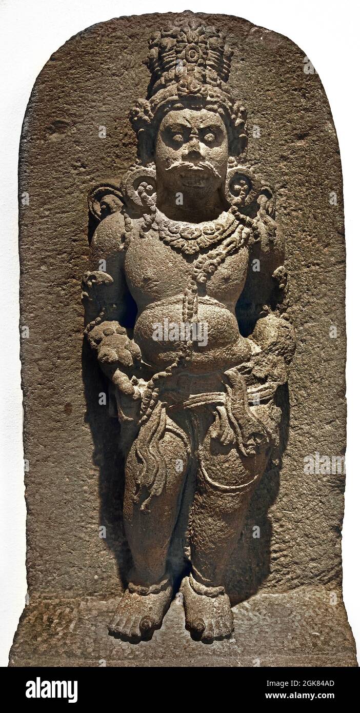 Mahakala, Türhüter des Shiva-Tempels. 800 - 900 Java Indonesia vulkanischer Stein 75× 37,5 × 21 ( Mahakala, der auf Shivas linker Seite steht. Seine dämonischen Eigenschaften – wildes Haar, wulstende Augen und offener Mund, ein fetter Körper und aufgerollte Zehen – machen ihn zum Gegenteil von der anmutigen Nandishvara. Sein Zeigefinger zeigt nach unten, auf die Gläubigen, die den Tempel betreten. ) Stockfoto