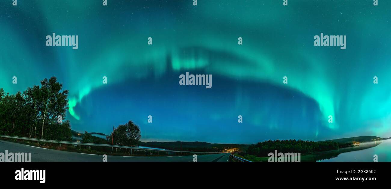 Panorama Aurora borealis, nördliche grüne Lichter mit Lot-Sternen am Nachthimmel über Bergstraße in Bergen, Spiegelung im Wasser, Nacht Stockfoto