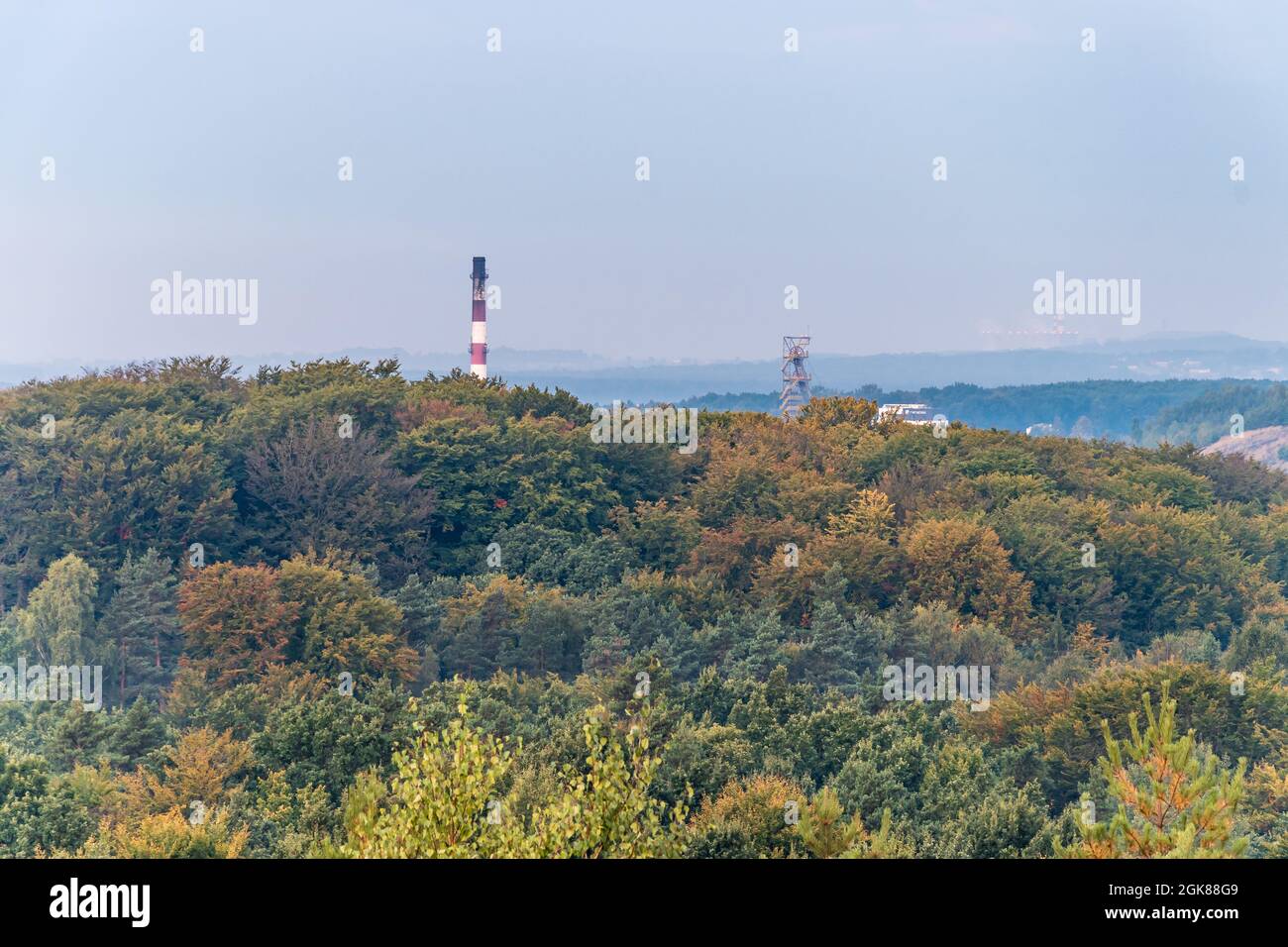 Der Turm des Minenschachts und der Fabrikschornstein bilden die Gipfel der Bäume, die durch die aufgehende Sonne aufgehellt werden. Luftaufnahme auf Herbstwald. Wald-, Fabrik- und Bergbauhaufen Stockfoto