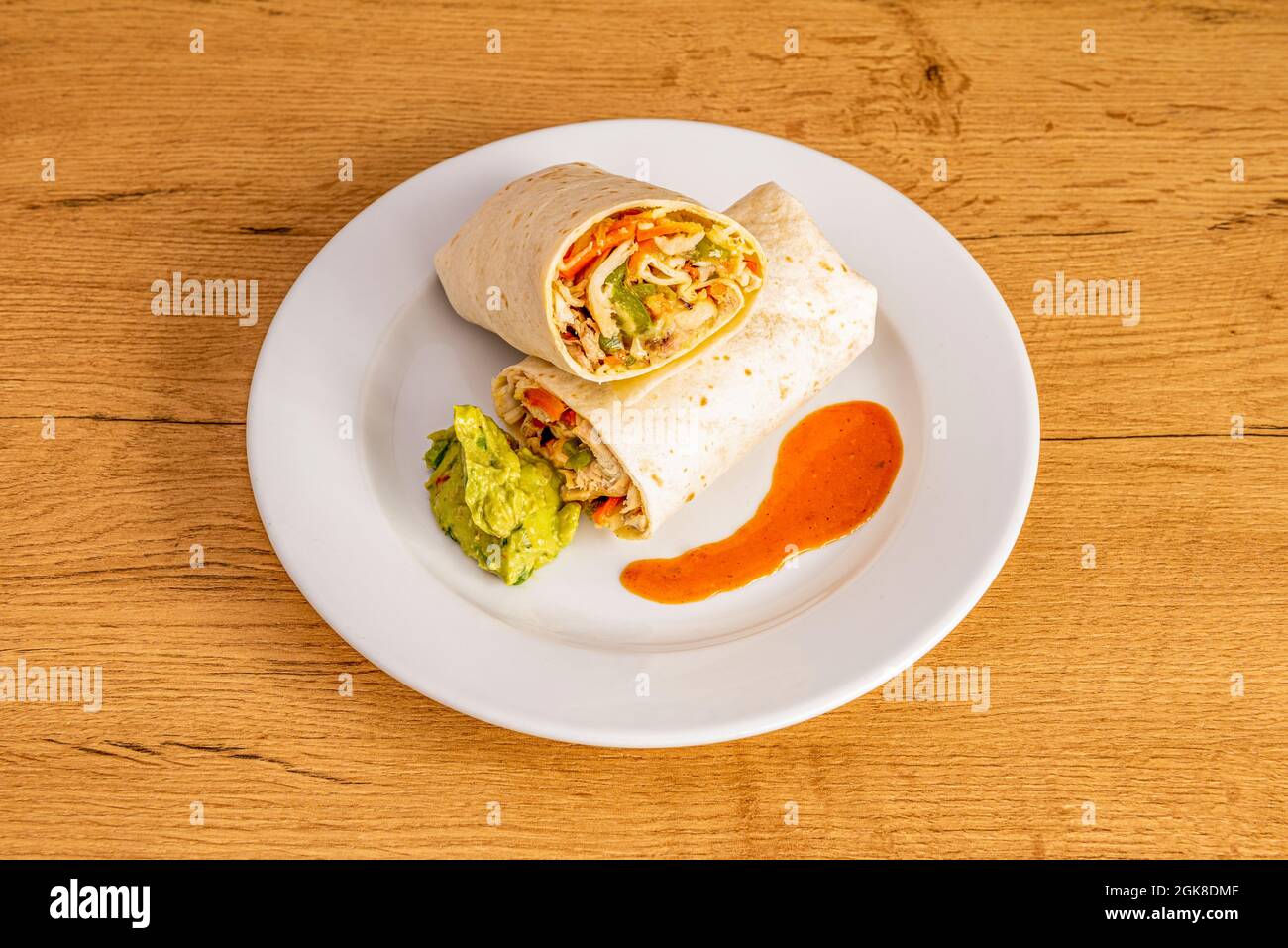 Burrito mit Weizentortilla mit Huhn und Guacamole auf weißem Teller und Holztisch Stockfoto