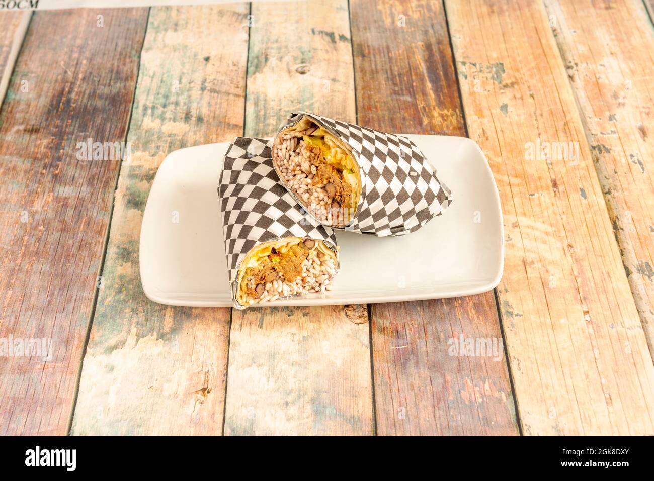 Mexikanischer Burrito mit weißem Reis, Bohneneintopf, Salat mit Gewürzen und Weiztortilla in kariertes Lebensmittelpapier verpackt Stockfoto