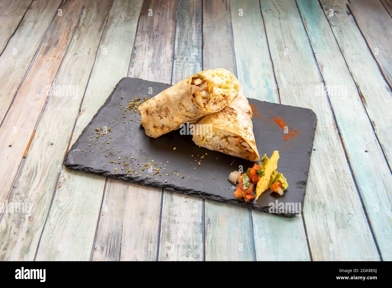 Beliebte mexikanische Weizen Tortilla Burrito Snack gefüllt mit Bohneneintopf und Huhn und weißem Reis mit Gemüse auf schwarzem Schieferteller Stockfoto