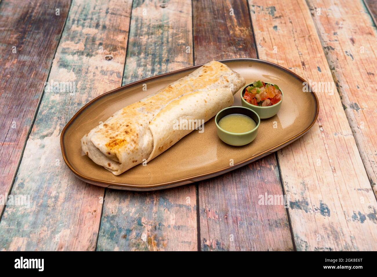 Große Präsentation von mexikanischen länglichen Burrito gefüllt mit Huhn, Reis und Bohnen mit dem Weizen Tortilla auf den Teller und Guranicion von Aji übergeben Stockfoto