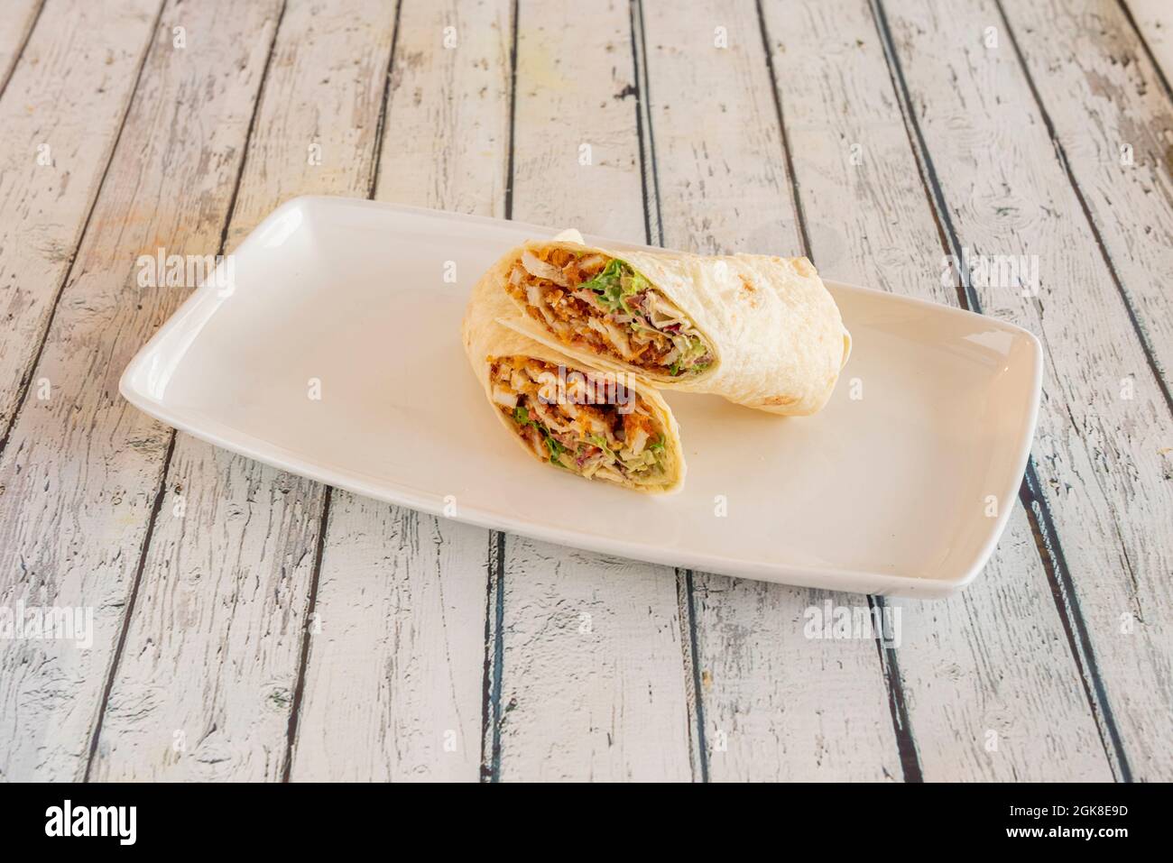 Gebratener panierter Hähnchen-Burrito mit einer Sauce aus Burrito mit Salat und Weizentortilla auf weißem Porzellanteller Stockfoto