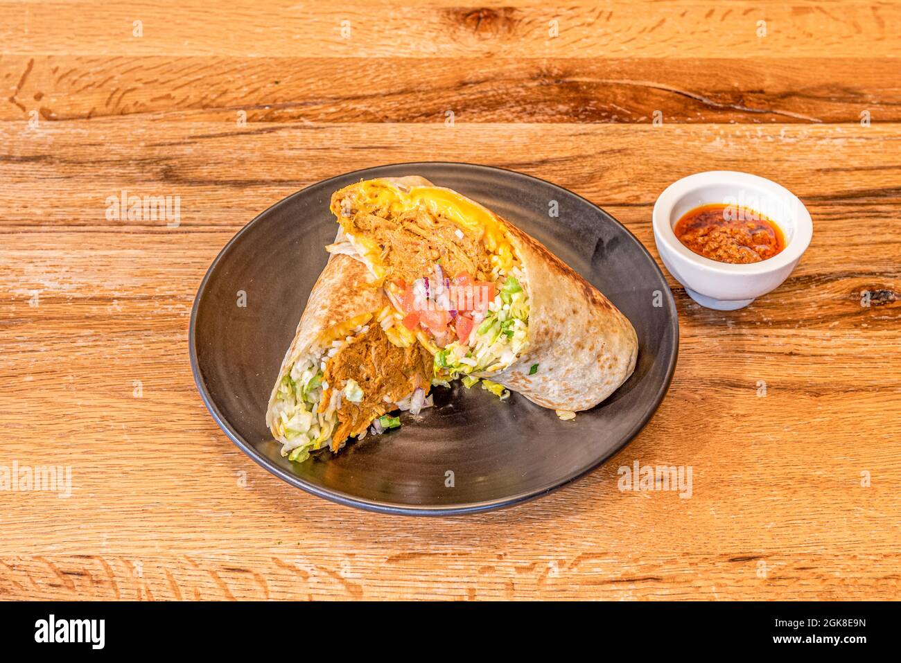 Cochinita pibil burrito mit viel weißem Reis und Salat, Cheddar-Käse und gegrillter Weizentortilla mit Sauce zum Eintauchen Stockfoto