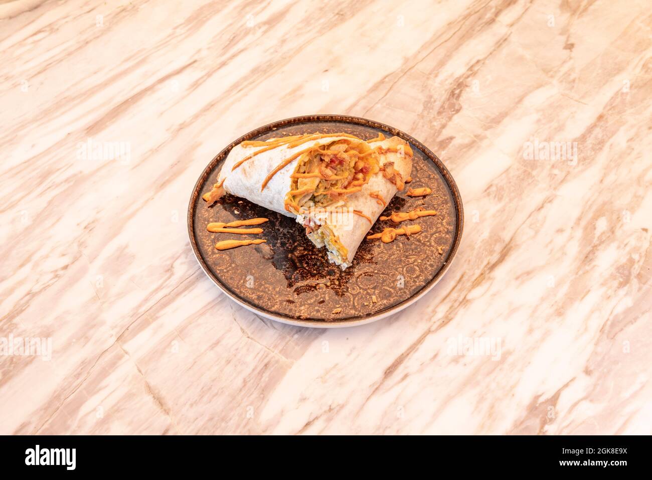Mexikanisches Hühnerburrito, umhüllt mit Weizentortilla und mit Streifen Cheddar-Sirup auf dem Marmortisch Stockfoto
