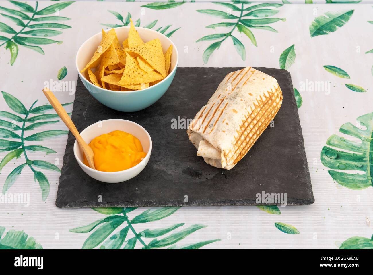 Corn Tortilla Burrito gefüllt mit Cheddar-Käse-Sauce und Bogen mit Mais-Chips auf einem schwarzen Schieferteller. Stockfoto