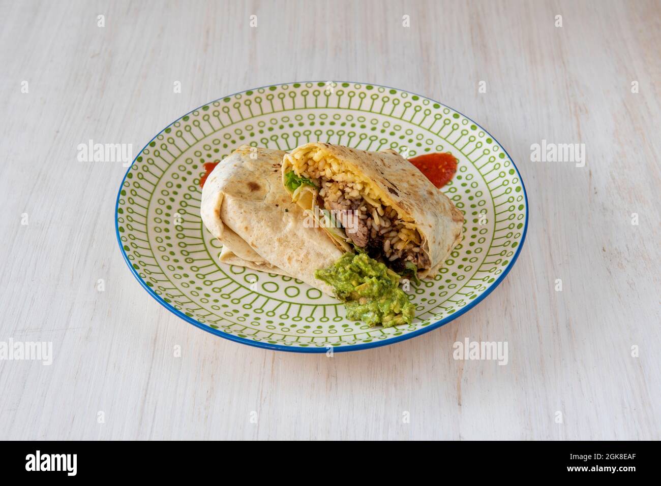 Weizentortilla Burrito gefüllt mit Chipotle-Huhn, Guacamole und Reis mit Saucen auf dekorierten Teller Stockfoto
