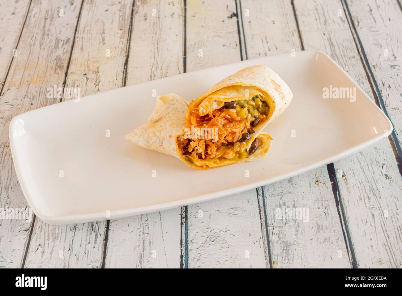 Mexikanisches Huhn Tinga Burrito mit Reis und Bohnen mit Weizentortilla und viel Sauce auf weißem Tablett Stockfoto