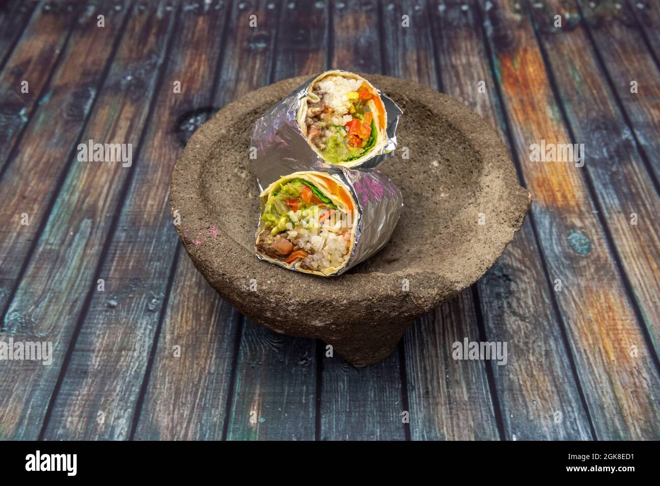 Veganer Burrito mit Reis und Gemüse und Weizentortilla in Aluminiumfolie auf mexikanischem Vulkangestein Molcajete eingewickelt Stockfoto