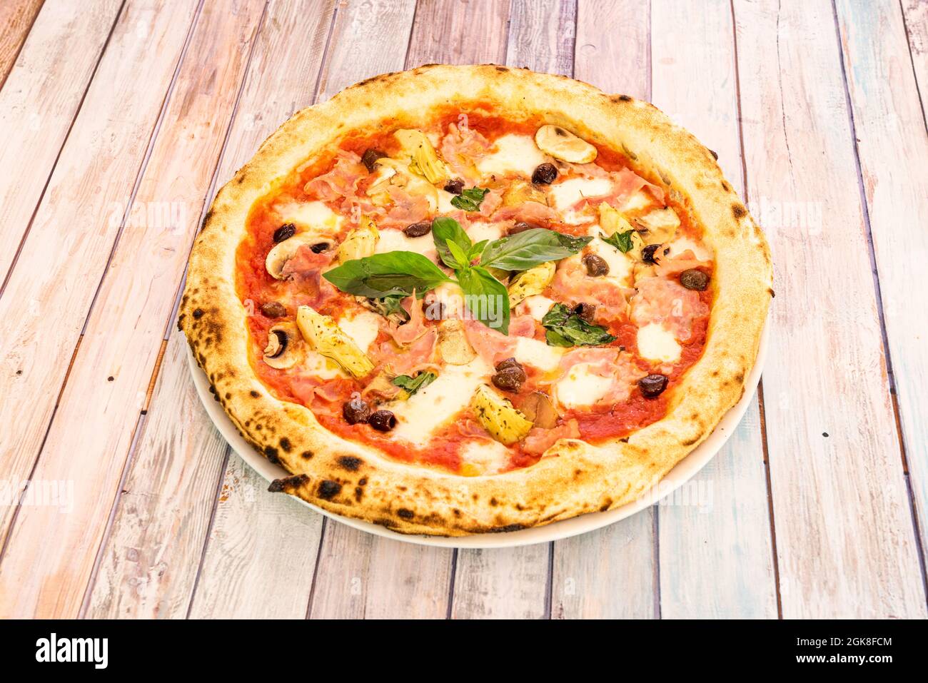 Skurrile italienische Pizza Rezept mit Artischockenherzen, Basilikum, Prosciutto, Schwarzen Oliven, Pilzen, Und Mozzarella-Käse Stockfoto