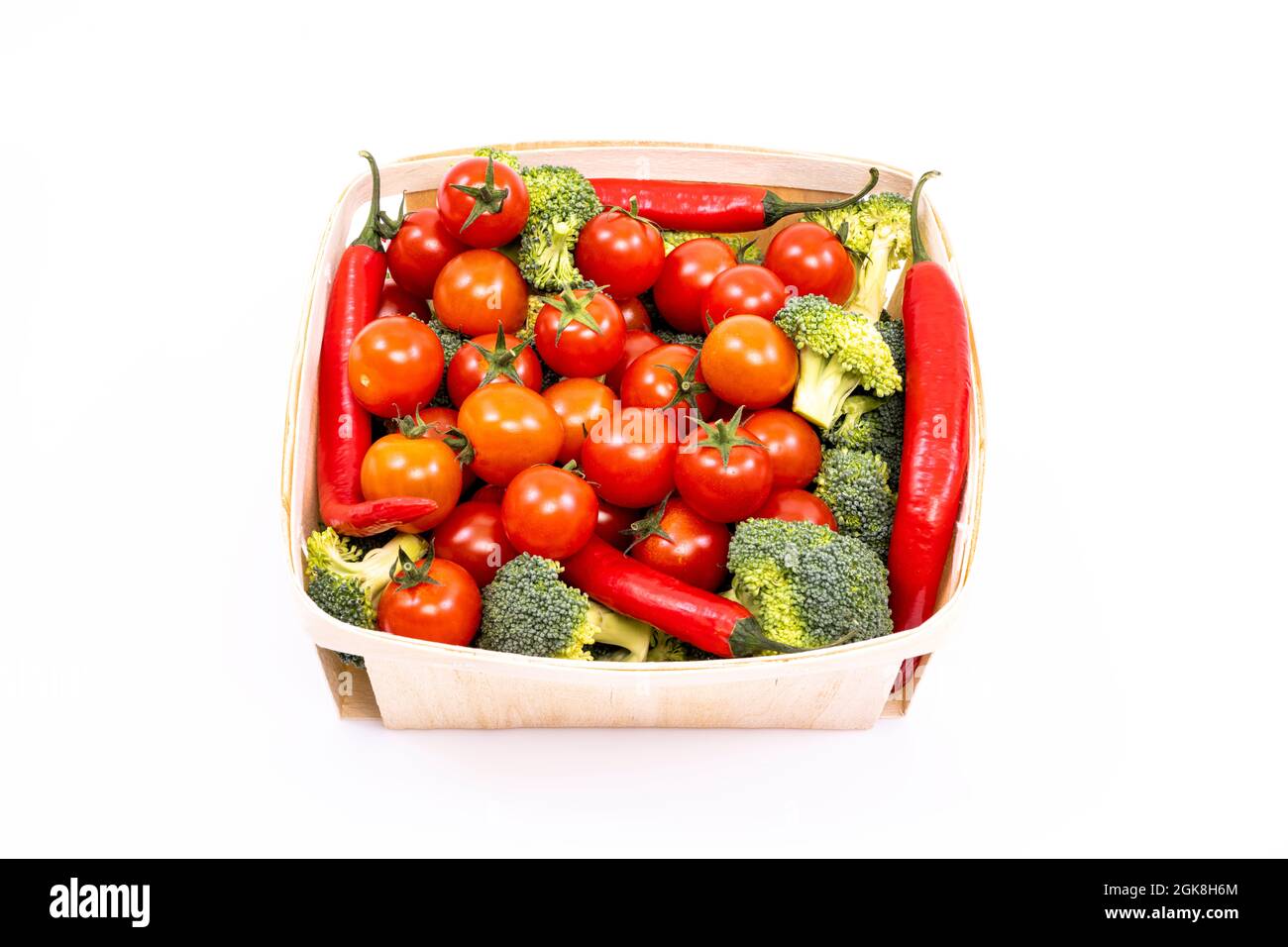 Dünnes Holztablett mit großen Kirschtomaten, Brokkoli-Stücken und roten Chili-Paprika auf weißem Hintergrund Stockfoto