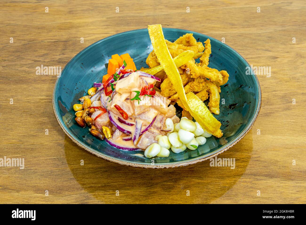 Schöne blaue Schale mit peruanischem corvina ceviche mit zerschlagenem Tintenfisch und Maiskörnern Stockfoto