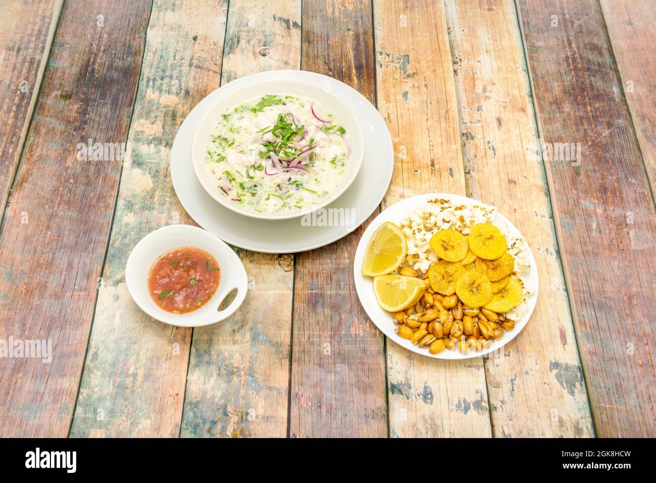 Weißer Fisch-Ceviche mit einer riesigen Hofgarnitur und einer Schüssel mit würziger Chilisauce auf einem Holztisch Stockfoto