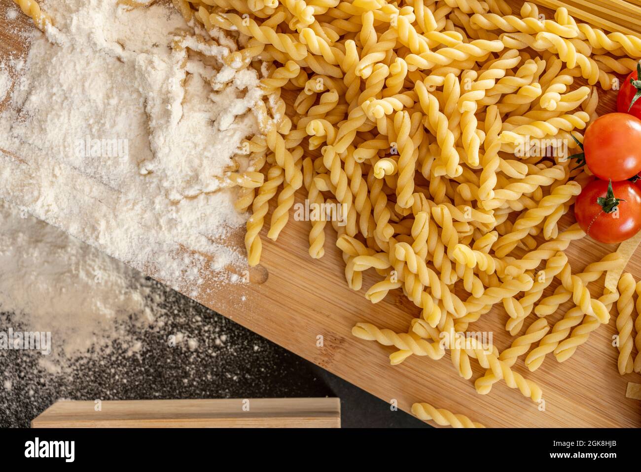 Draufsicht Bild von roher italienischer Pasta, Weizenmehl, Kirschtomaten und Bambus-Tisch auf schwarzem Hintergrund Stockfoto