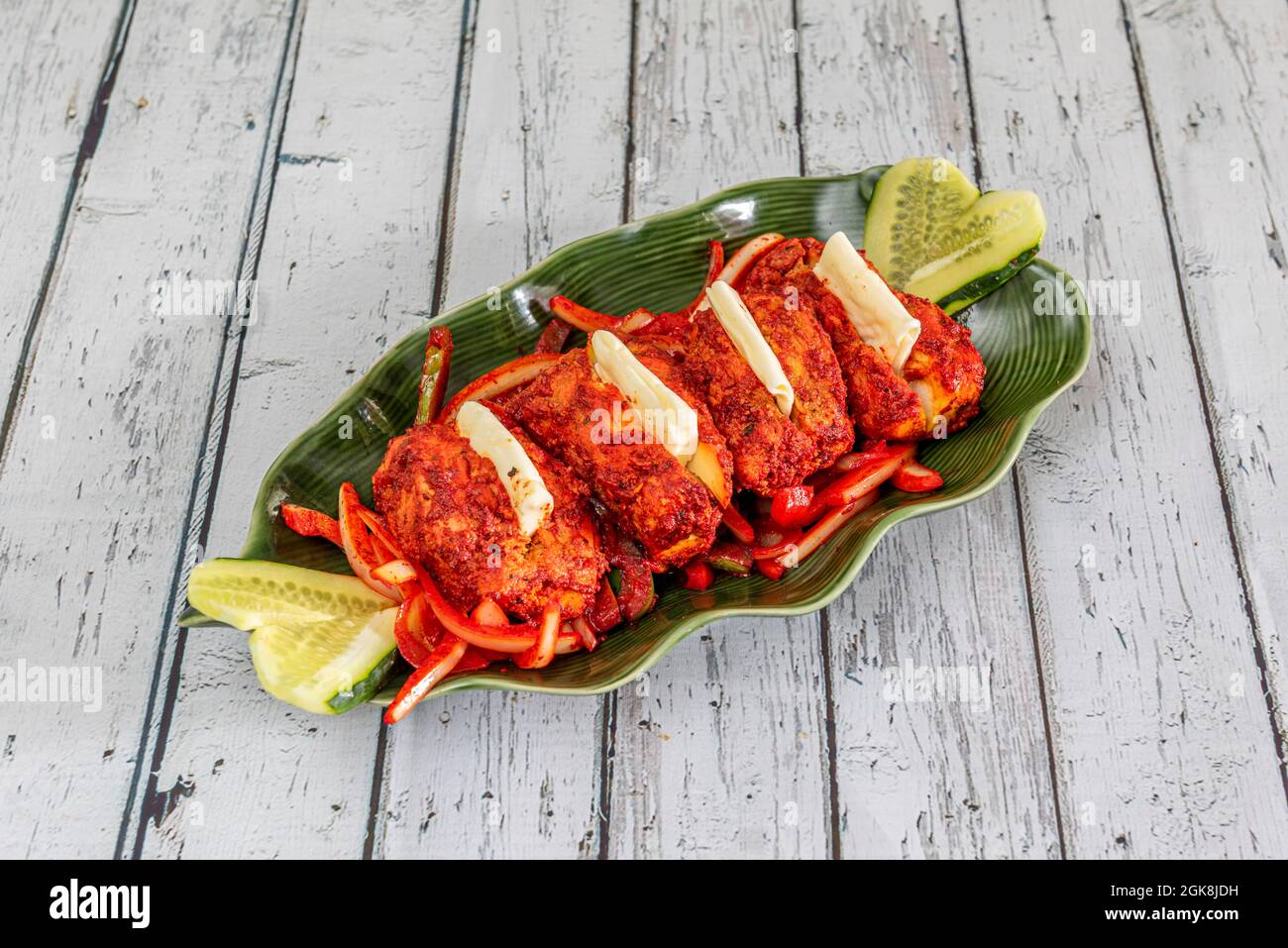 Tablett mit köstlichen indischen gebratenen Huhn Tikka Rezept mit Gemüse und Gurke auf grün belaubten Tablett Stockfoto