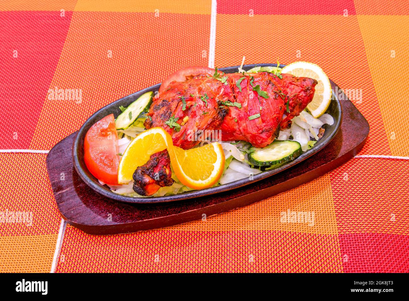 Gegrillter Hähnchenschenkel im Hindu-Tandoori-Stil mit leuchtend roter Farbe und verkohlten Grillmarkierungen auf der heißen Platte und dem orangefarbenen Tisch Stockfoto