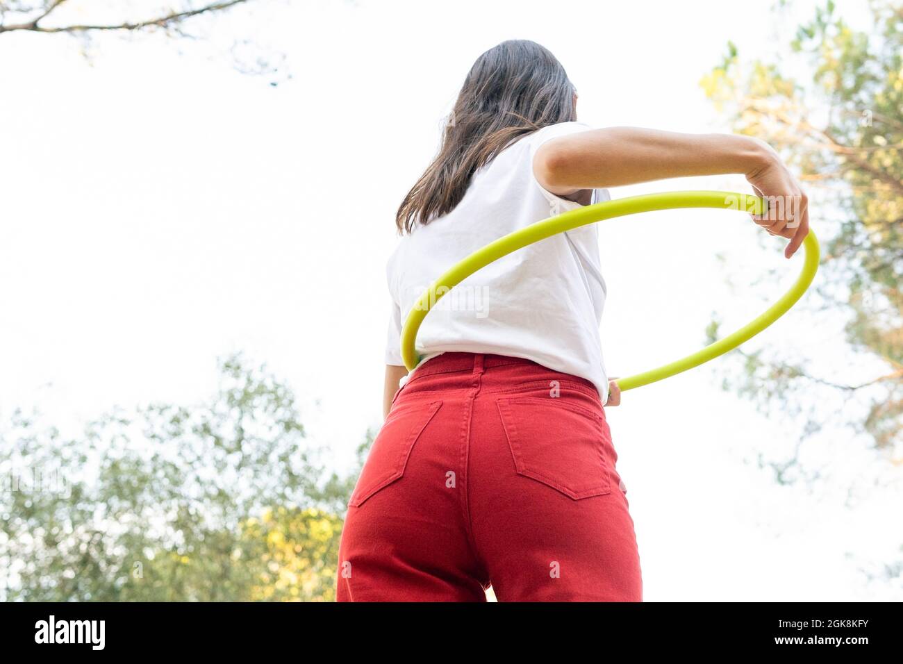 Von unten Rückansicht eines nicht erkennbaren weiblichen Teenagers in roten Jeans, der Hula Hoop hält, während er Freizeit im Park hat Stockfoto