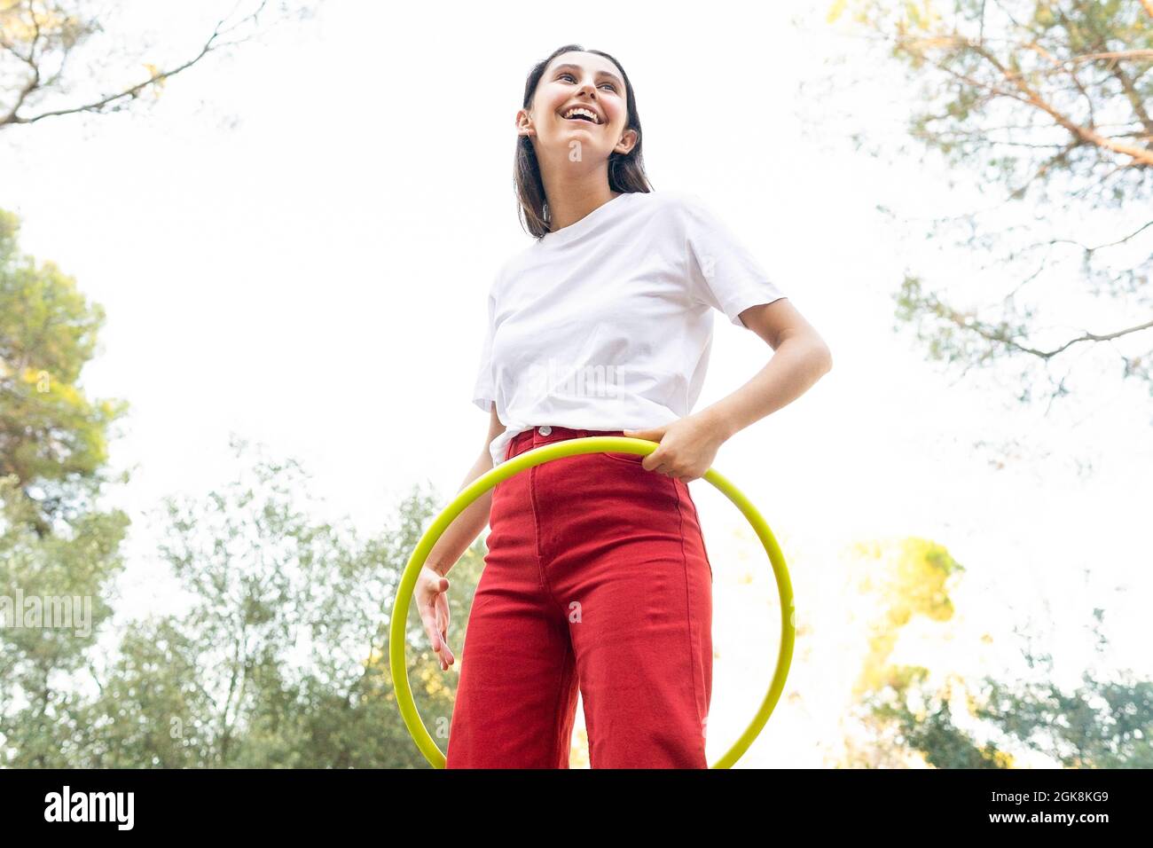 Von unten fröhliche weibliche Teenager in roten Jeans wirbelnden Hula Hoop Reifen während der Freizeit im Park Stockfoto