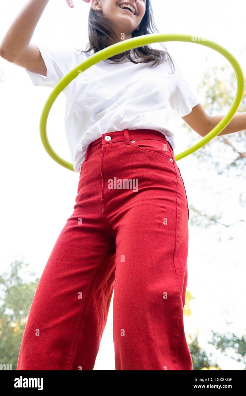 Von unten der Ernte unkenntlich fröhlich weiblichen Teenager in roten Jeans wirbelnden Hula Hoop Reifen während mit Freizeit im Park Stockfoto