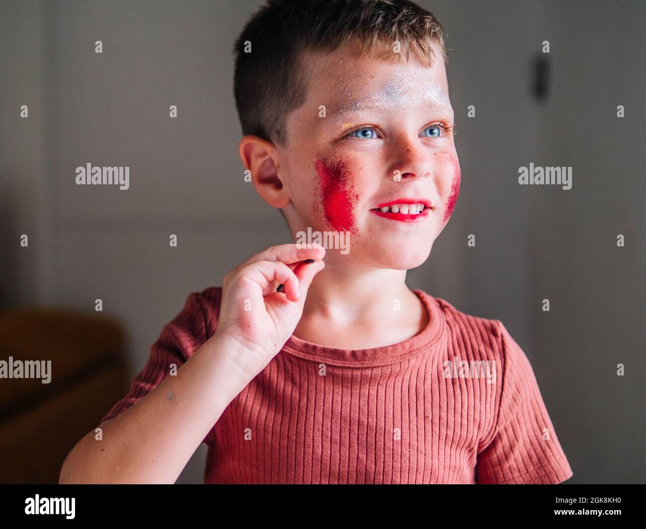 Unordentliches Kind mit braunen Haaren und Kosmetik im Gesicht im hellen Haus auf verschwommenem Hintergrund Stockfoto