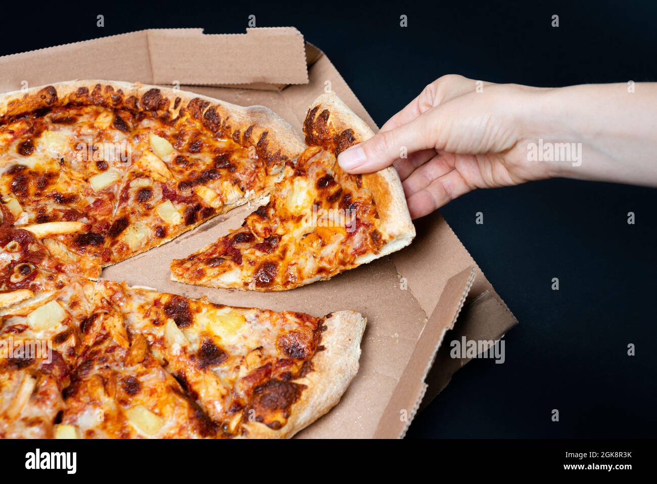 Hand nehmen ein Stück Pizza aus der Pizza-Box. Große Hawaii Pizza ohne ein Stück. Blick von oben auf Hawaii Pizza. Konzept für italienisches Essen, Street Food, Fast Stockfoto