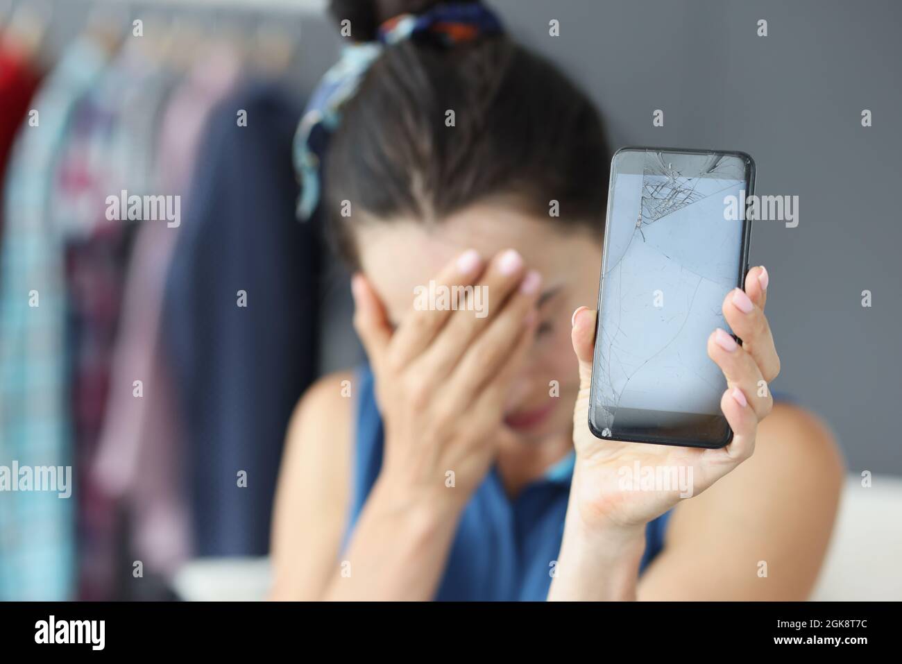Traurige Frau, die ihre Augen mit der Hand bedeckte und das zerbrochene Handy in Nahaufnahme hielt Stockfoto