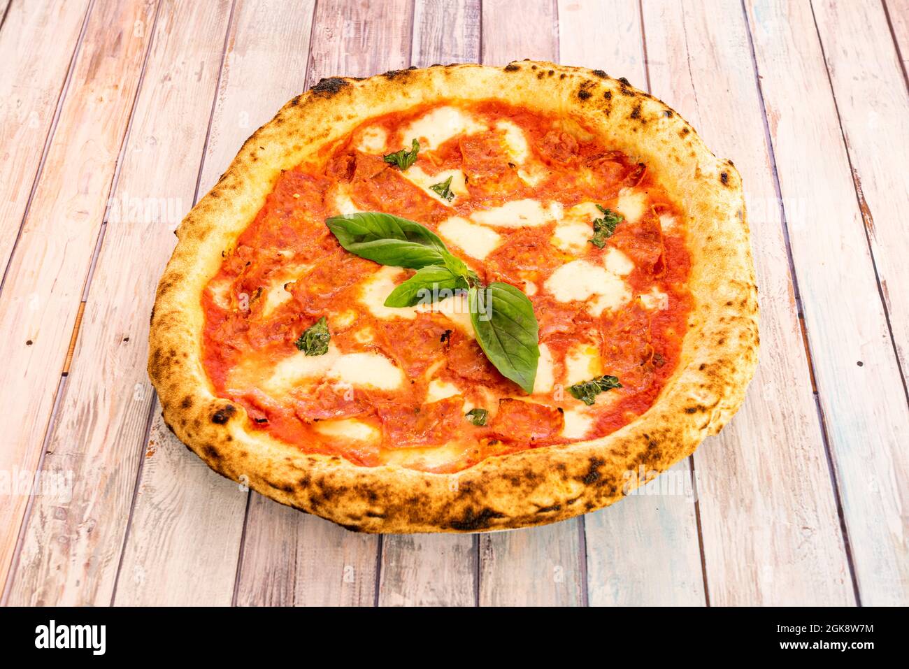 Kleine Pizza mit superfeinem Mehlteig mit viel scharfem Chorizo und Basilikumstücken darauf. Stockfoto