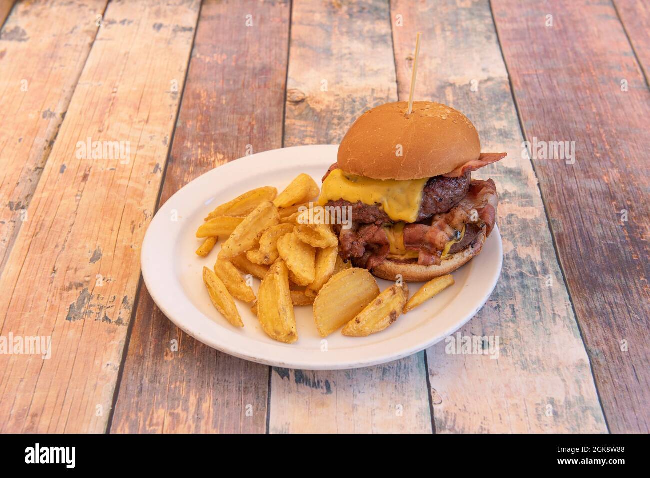 Double Beef Burger mit gebratenem Speck, geschmolzenem Cheddar-Käse mit Tomate und Senf garniert mit Pommes frites Stockfoto