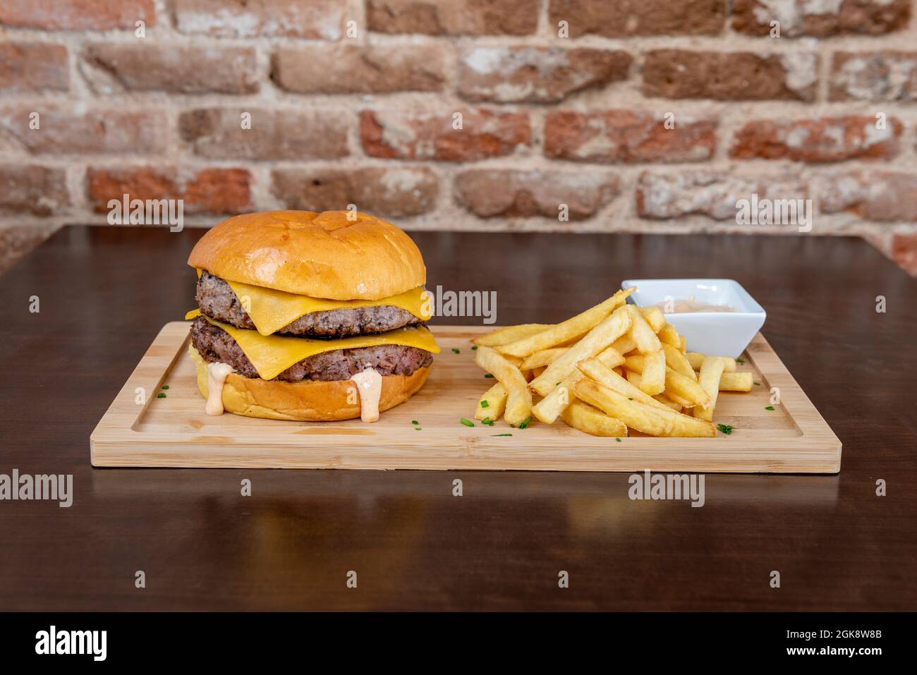 Double Burger mit geschmolzenem Cheddar-Käse und Mayonnaise-Sauce, garniert mit Pommes auf Holzbrett Stockfoto